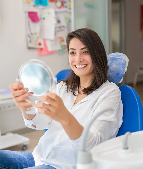 Smiling woman in dental chair holding a mirror, admiring her tooth-colored fillings at Sipes Dental in York, PA.