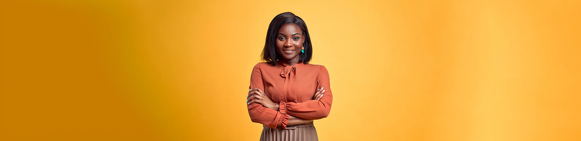 Smiling woman in a brown blouse with arms crossed, standing against a bright yellow background, representing confidence and professionalism in a dental practice context.
